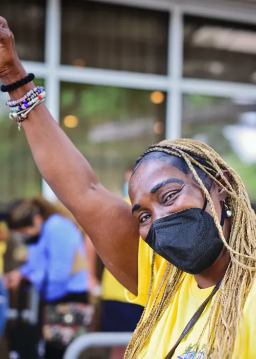 masked person with braids, raised fist in the air