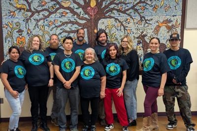 Several people posed wearing shirts with logos in front of tree mural