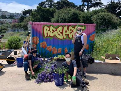 Three people around bunch of cut flowers, in front of graffiti word "respect"