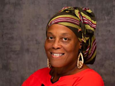 Photo portrait of a Black woman smiling with a patterned head wrap and a bright red shirt