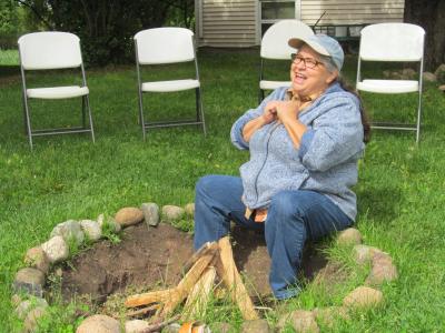 woman in ballcap and jeans, seated at a fire pit
