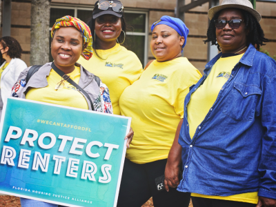 four smiling activists in yellow shirts, holding sign 