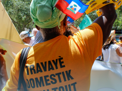 person facing away from camera, fist in air, orange shirt and headwrap