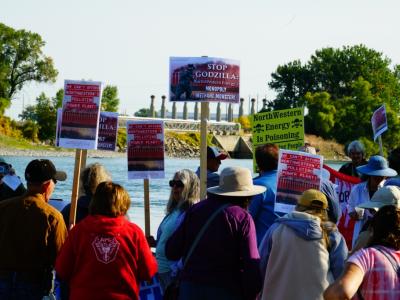 crowd of people with signs in foreground, water and factory in background