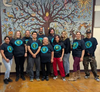 Several people posed wearing shirts with logos in front of tree mural