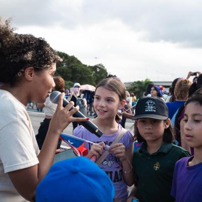 young person with microphone talking to kids in a crowd